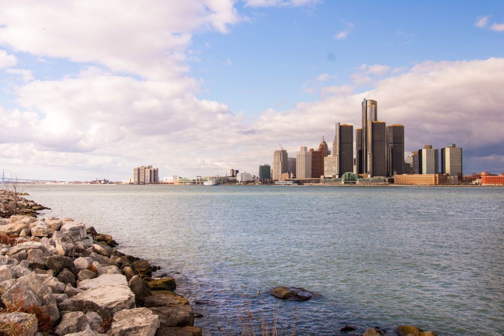 Detroit skyline as seen across the lake from Canada. Shiny tall skyscrapers against a pretty blue sky. in the foreground, rocks on the beach on the shore of the lake.