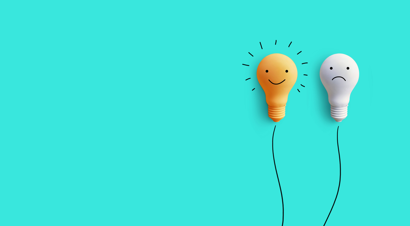 two light bulb shaped balloons against a blue-green background. one bulb is orange and has a happy face and glow. the other is white and sad.