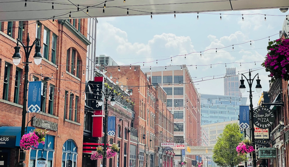 Greektown in Detroit. A street with lights strung across it on a sunny day. The sign for Greektown Casino can be seen on the left. Detroit Online Casinos Remain $20 Million in Monthly Revenue Ahead of Tribal Rivals