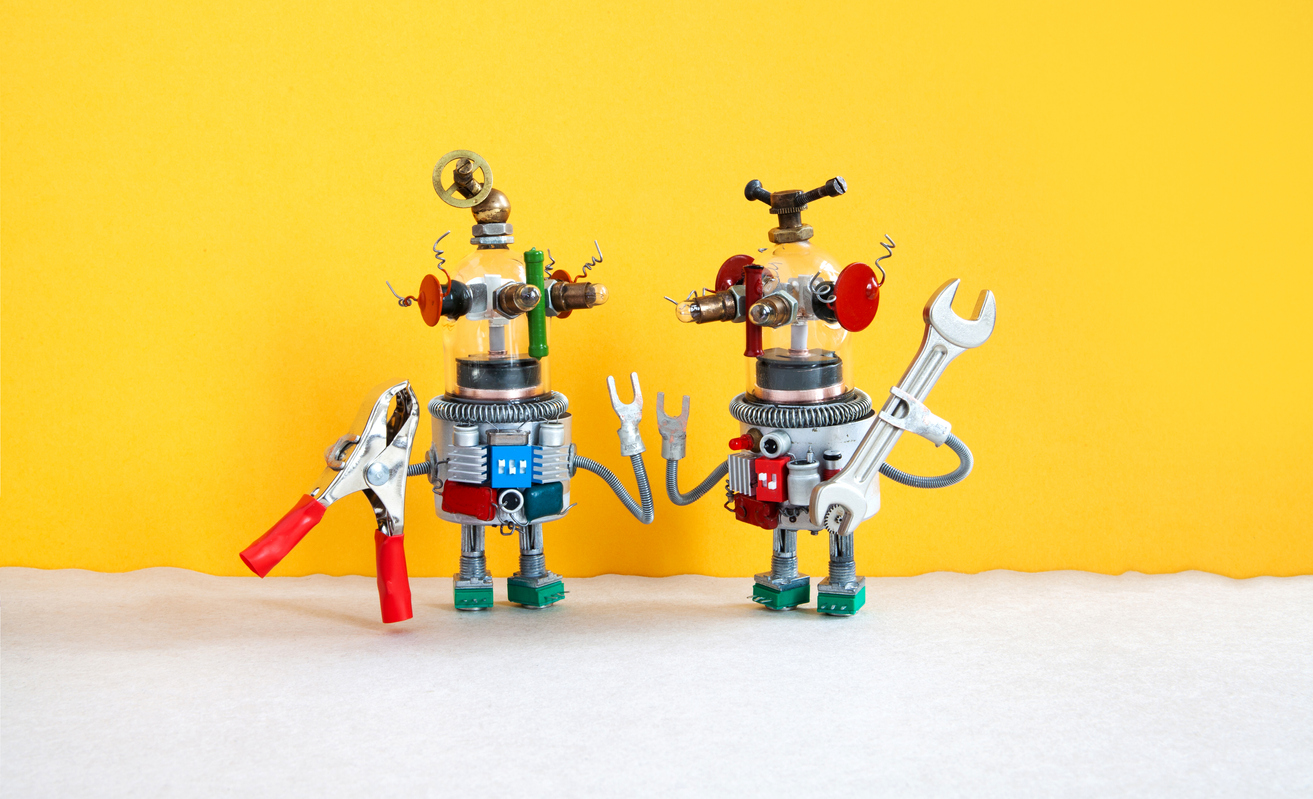 A yellow wall with 2 robots standing in front of it, holding tools. the robot on the left holds clamps and the robot on the right holds a wrench.